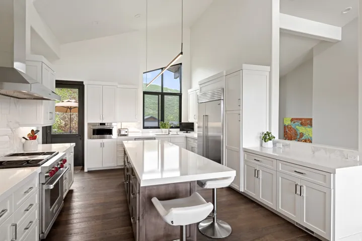Open-concept kitchen featuring a large central island, white cabinetry, dark wood-finish flooring, stainless steel appliances, and high vaulted ceilings