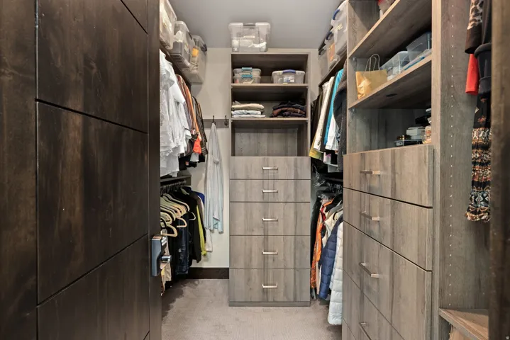 Custom closet system featuring dark wood-finish cabinetry, light wood-finish shelving, and integrated drawer storage with brushed metal pulls