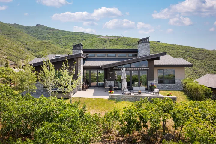 Modern mountain residence featuring a multi-level patio, stone accent walls, and a prominent chimney
