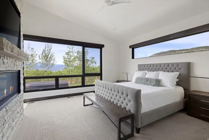 Spacious bedroom featuring large picture windows, a linear fireplace with stone surround and stone mantel, a vaulted ceiling, and recessed lighting