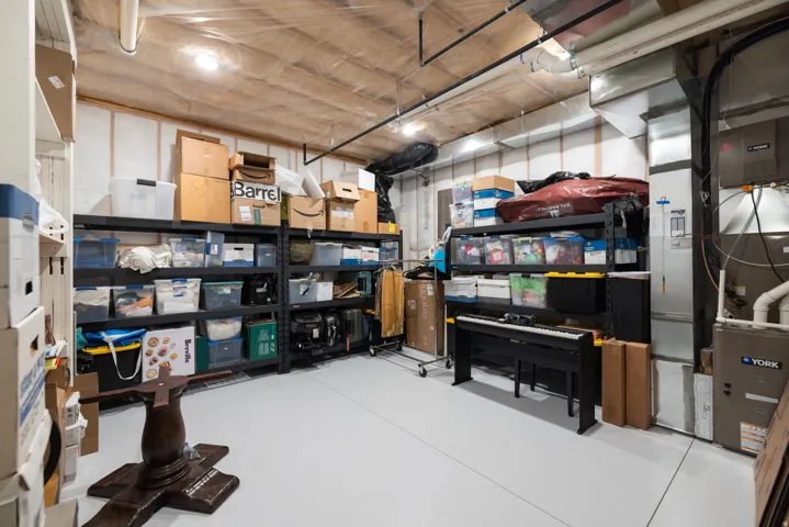 Finished basement storage room featuring painted concrete flooring, exposed ceiling joists, and utility access