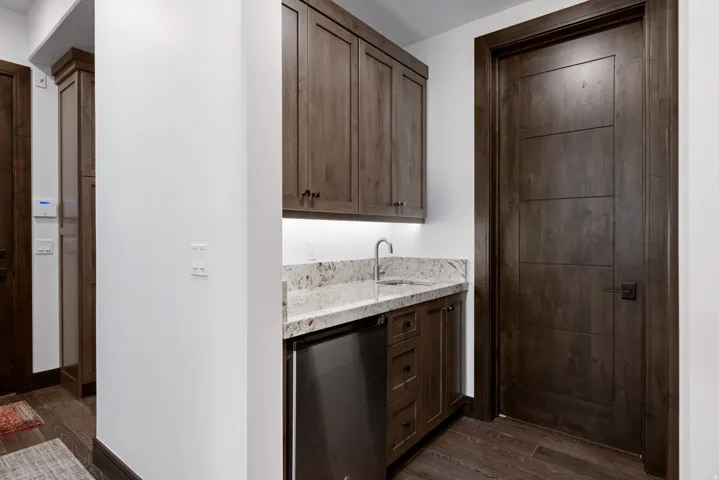 Wet bar featuring dark wood cabinetry, a light-toned granite countertop, and a stainless steel sink with a gooseneck faucet