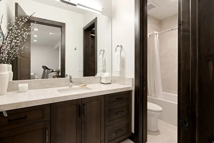 Bathroom featuring a large vanity with a light-toned countertop, integrated rectangular sink, dark wood-finish cabinetry with black hardware, and a framed mirror with overhead lighting