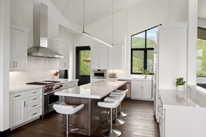 Vaulted kitchen featuring white cabinetry, a large center island with seating, dark wood-finish flooring, and a stainless steel appliance suite