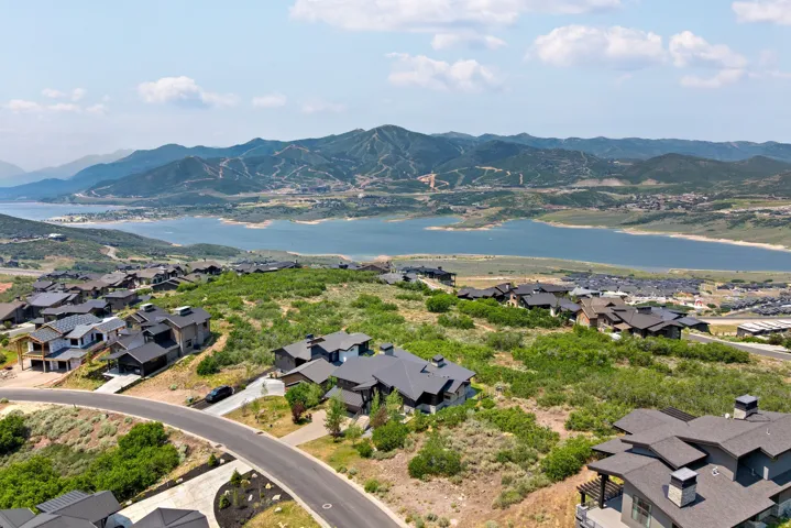 Expansive landscape featuring an elevated residential area with modern homes, a tranquil lake, and distant mountains