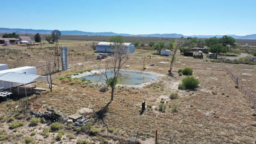 Expansive rural property featuring a large pond, a traditional windmill structure, and multiple outbuildings including a covered shed and a Quonset hut