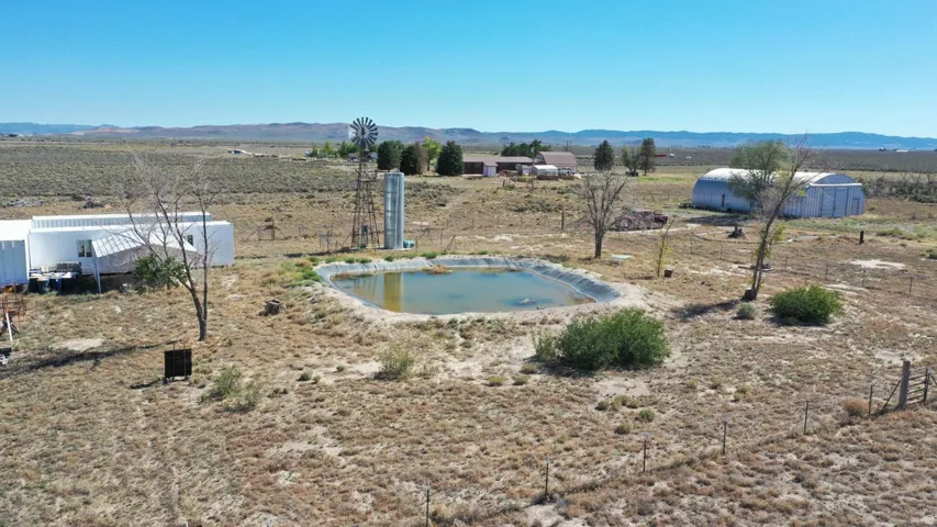 Expansive parcel featuring a pond, windmill, and multiple outbuildings, including a large white structure and a quonset hut