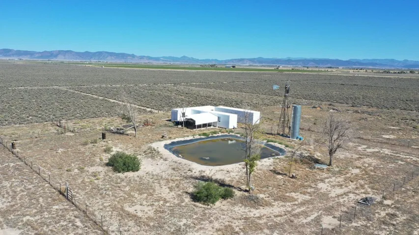 Expansive rural property featuring a large pond, a modern single-story residence, a classic windmill structure, and a cylindrical storage tank