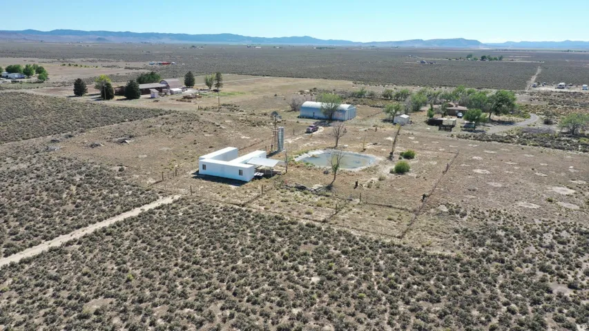 Expansive rural property featuring a white contemporary structure, a wind turbine, an adjacent pond, a large metal barn, and additional outbuildings
