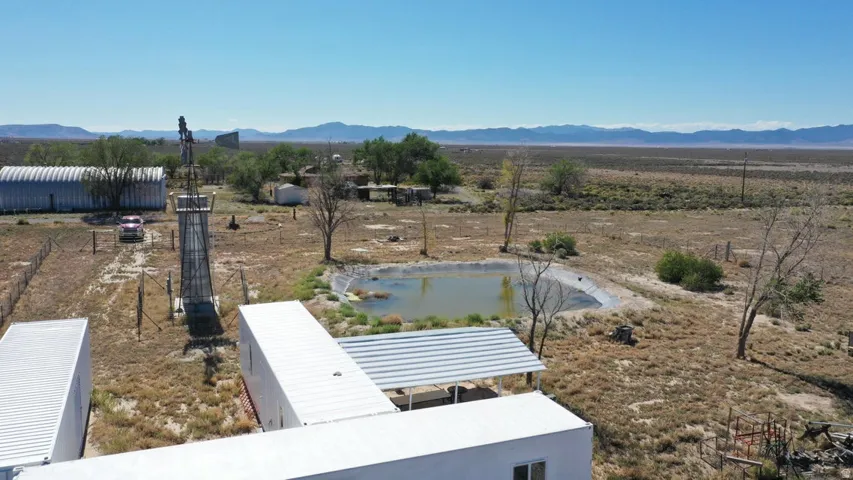Expansive desert property featuring multiple outbuildings, a water retention pond, and a large metal windmill structure