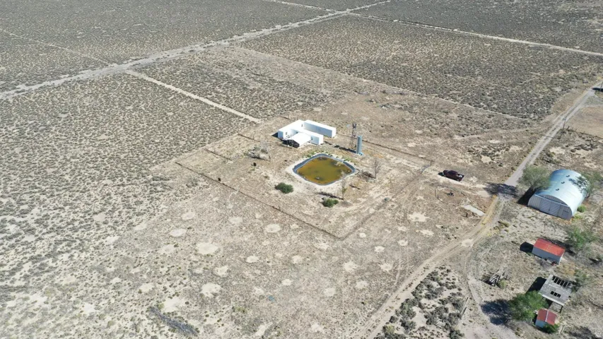Expansive arid landscape featuring multiple buildings, a large Quonset hut structure, a water feature, and extensive land divisions