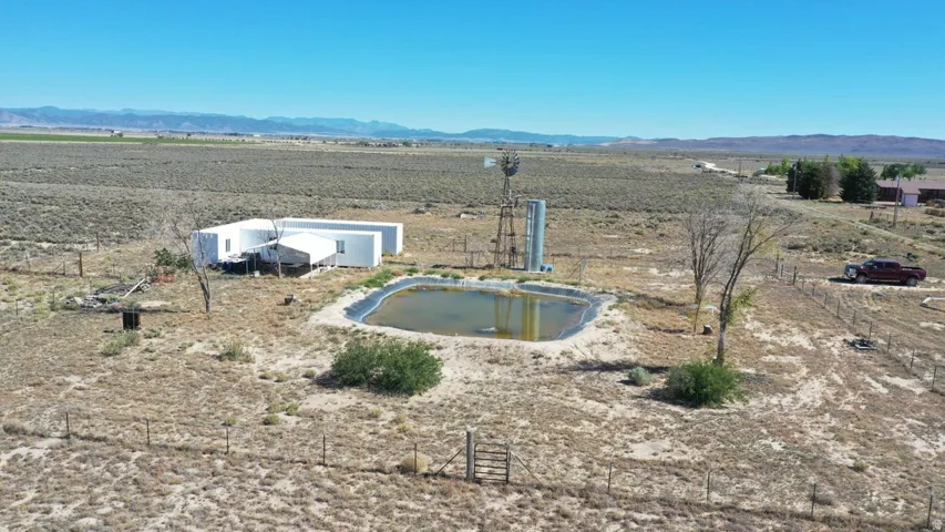 Expansive rural property featuring a modern white structure, a large pond, a traditional windmill, and a fenced perimeter