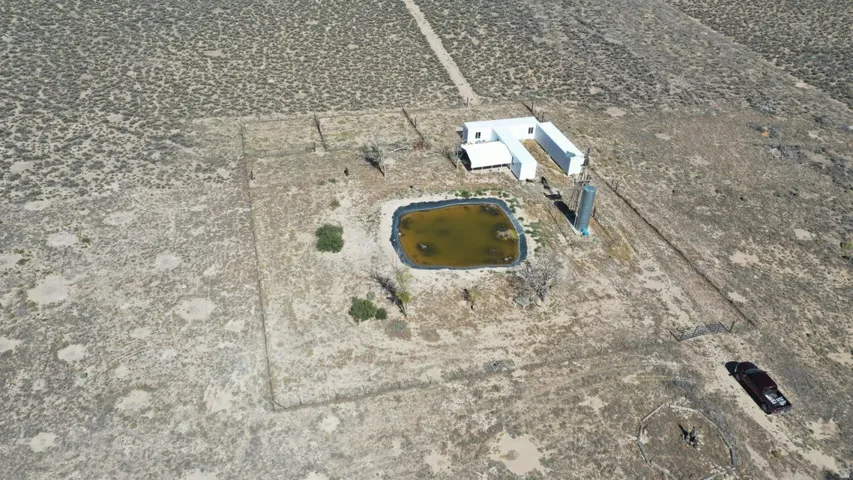 Expansive desert property featuring a pond, a white-sided single-story structure, and multiple outbuildings