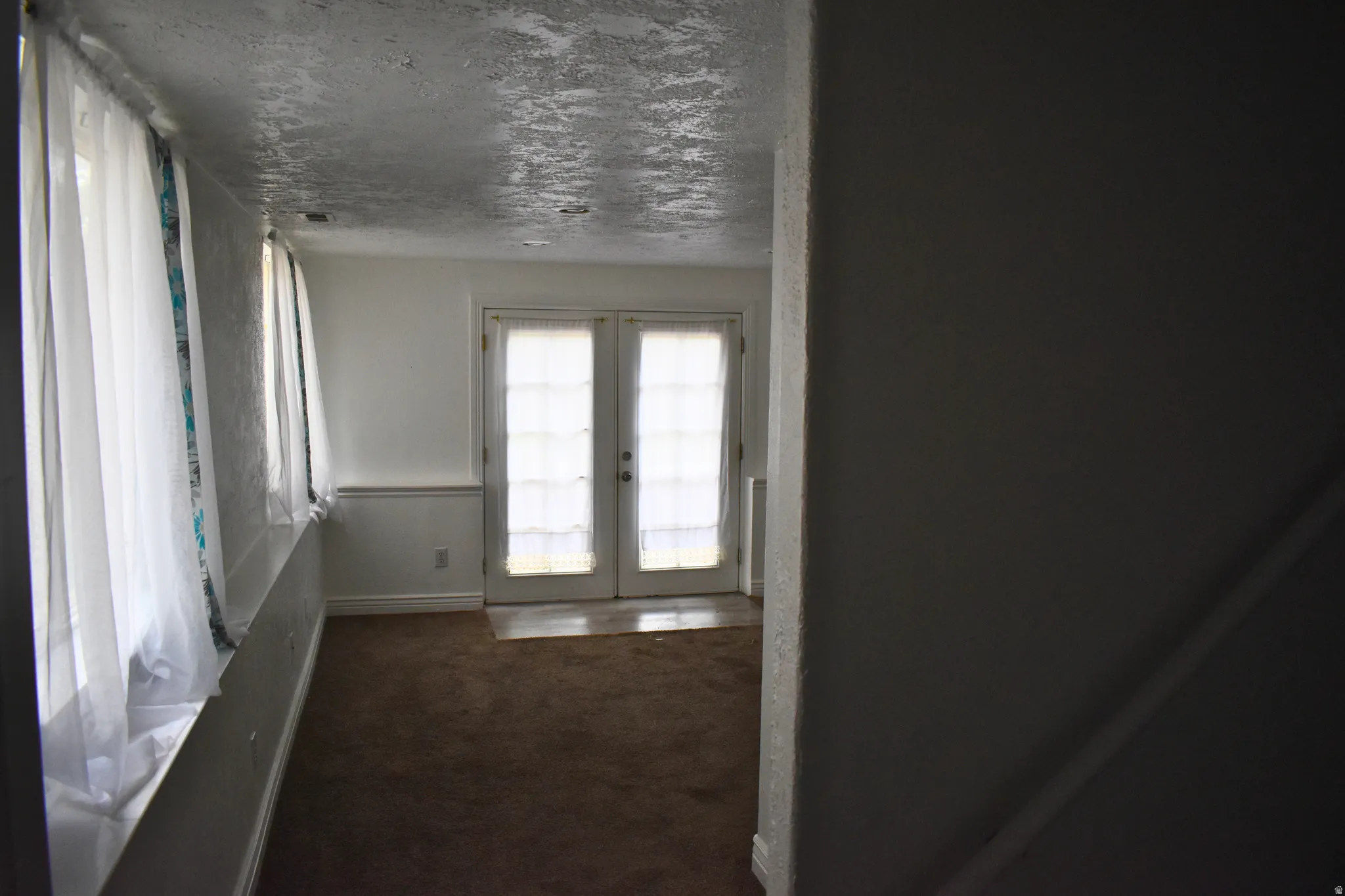 Carpeted room with a wall of sheer-draped windows and a pair of French doors