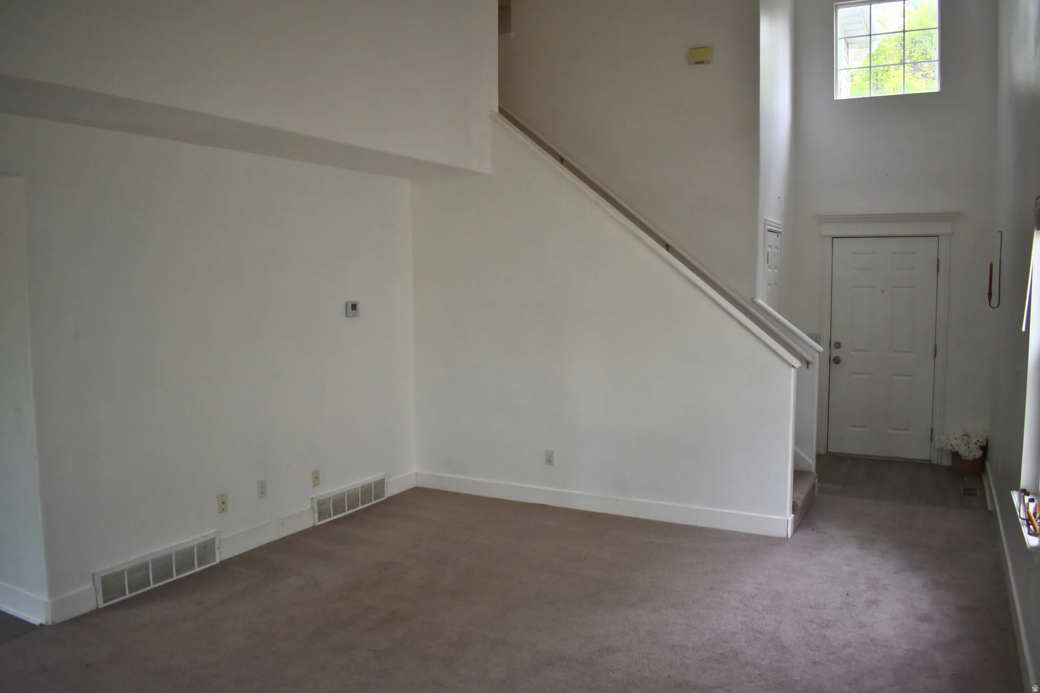 Two-story foyer with high ceilings, featuring a multi-pane window, staircase with a handrail, and a paneled entry door
