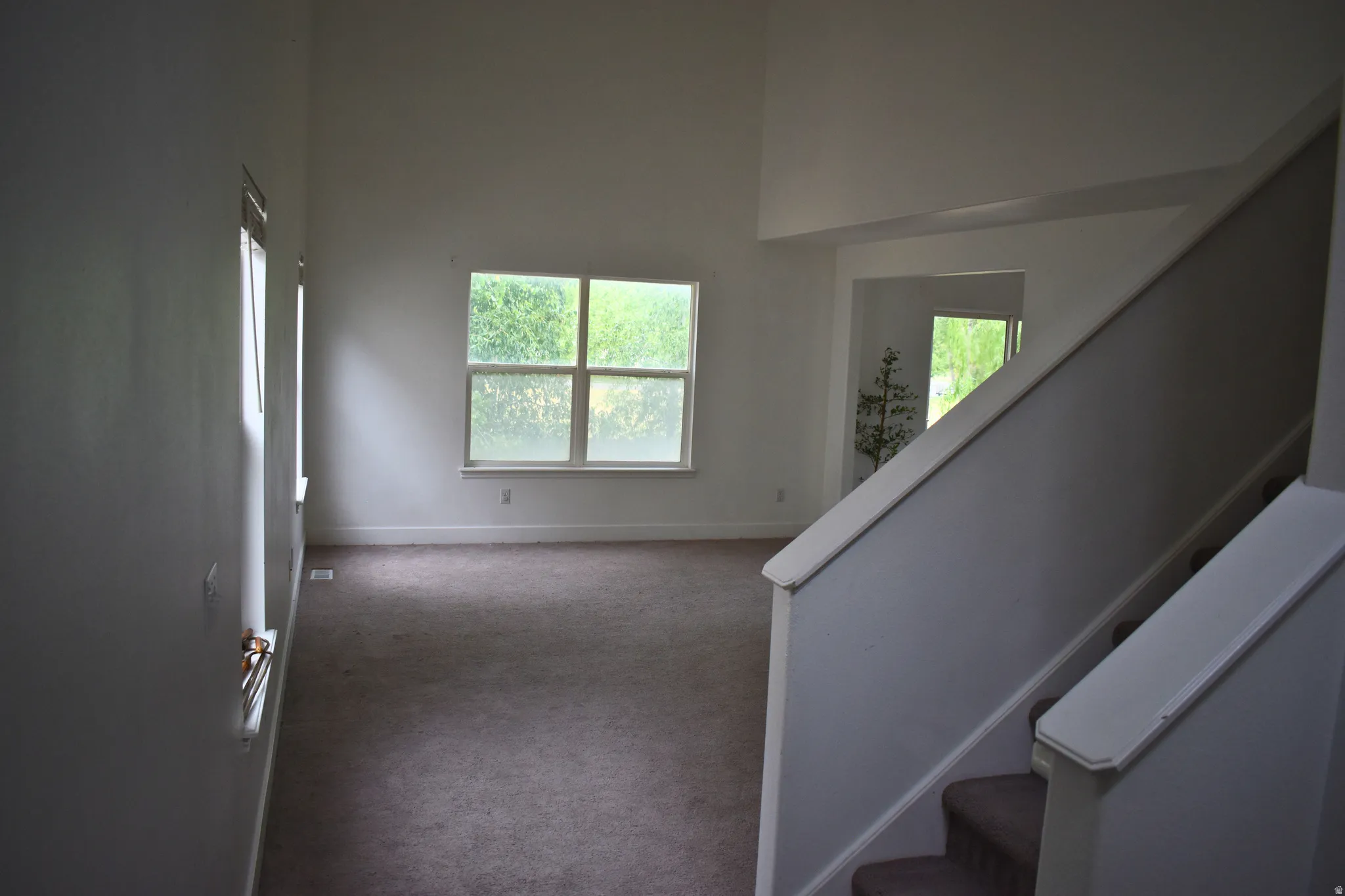 Open concept living space featuring a two-story ceiling, multiple windows, and carpet flooring