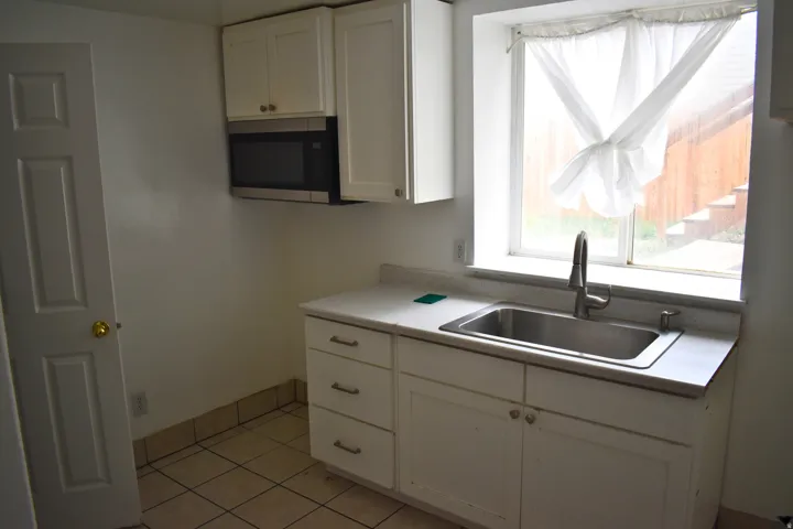 Kitchenette featuring white cabinetry, a stainless steel sink with a modern faucet, an over-the-range microwave, and light-colored tile flooring