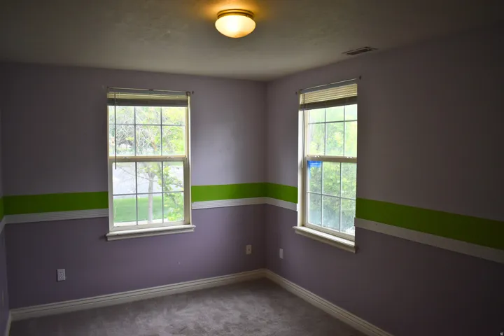 Carpeted interior room featuring two double-hung windows with blinds, a flush-mount ceiling light fixture, and baseboard trim