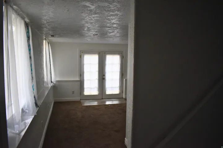 Carpeted room with a wall of sheer-draped windows and a pair of French doors
