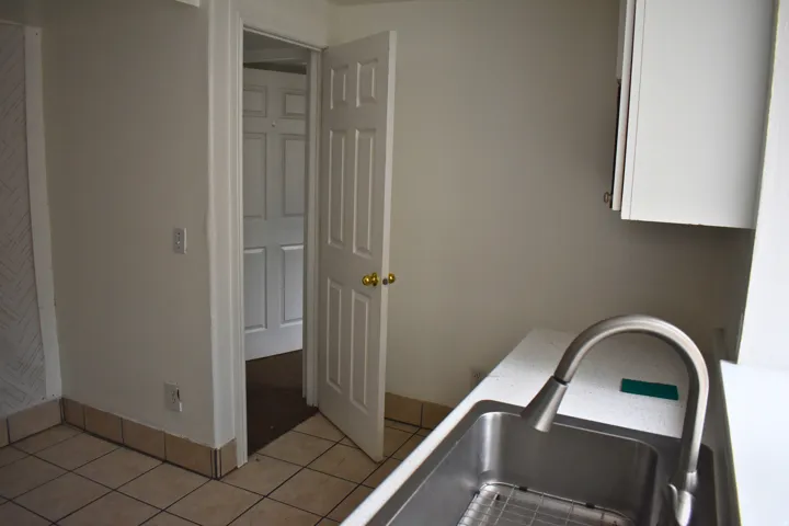 Kitchen area featuring a stainless steel undermount sink with a high-arc faucet, white upper cabinetry, and a light-toned countertop