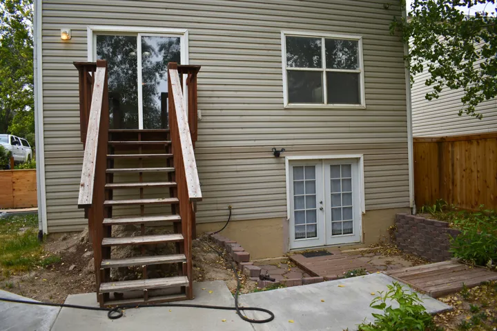 Rear exterior with light-colored siding, featuring a wooden deck with stairs leading to a sliding glass door