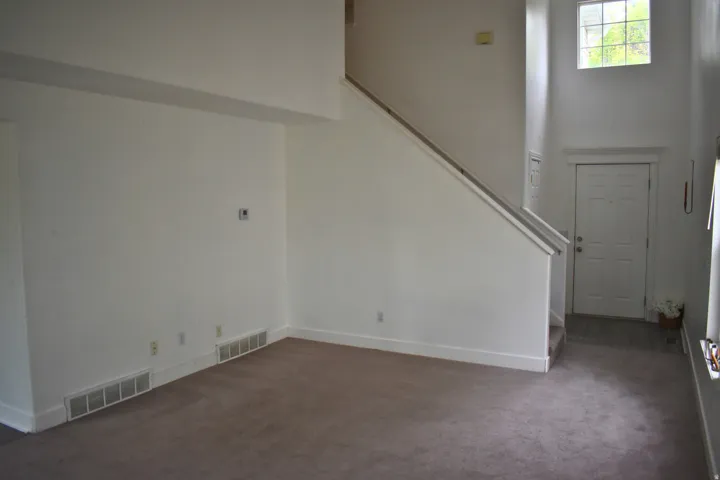Two-story foyer with high ceilings, featuring a multi-pane window, staircase with a handrail, and a paneled entry door