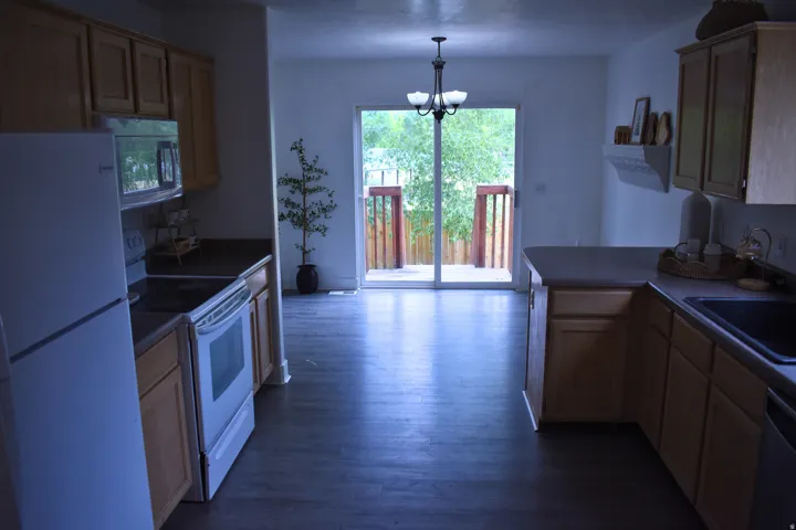 Kitchen featuring wood-finish flooring, light wood cabinetry, white appliances, and a sliding glass door leading to an outdoor deck with wood railings