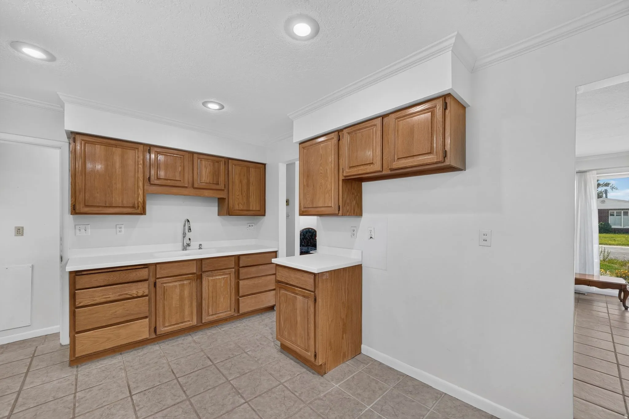 Kitchen featuring light wood cabinetry, white countertops, a stainless steel faucet, recessed lighting, and tiled flooring