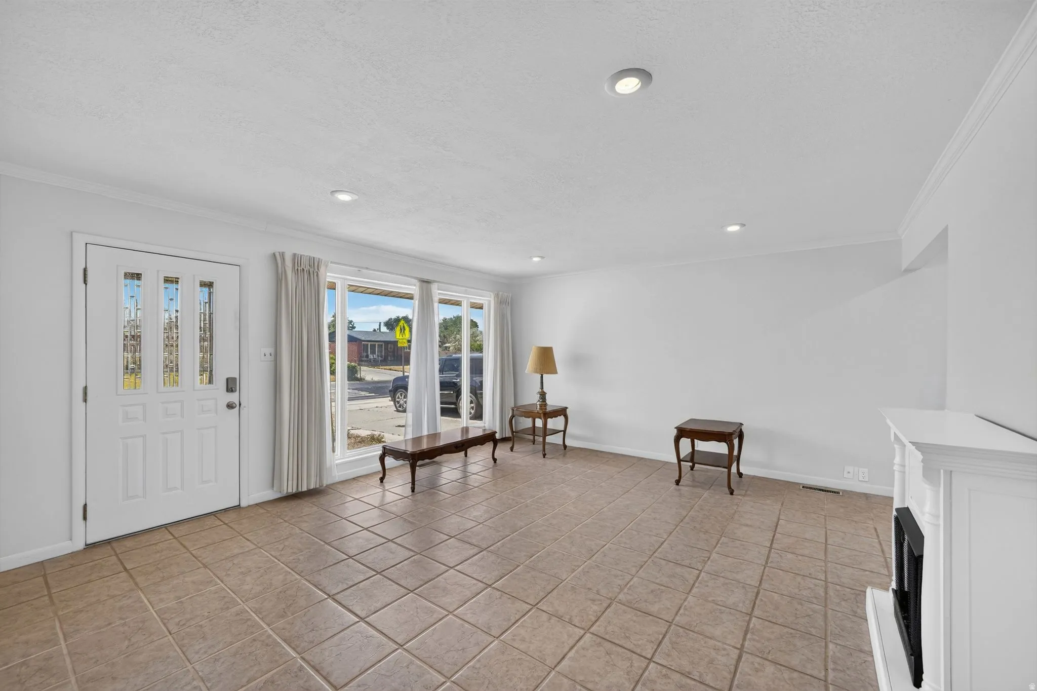Spacious living area featuring neutral-toned tile flooring, recessed lighting, and a white decorative fireplace