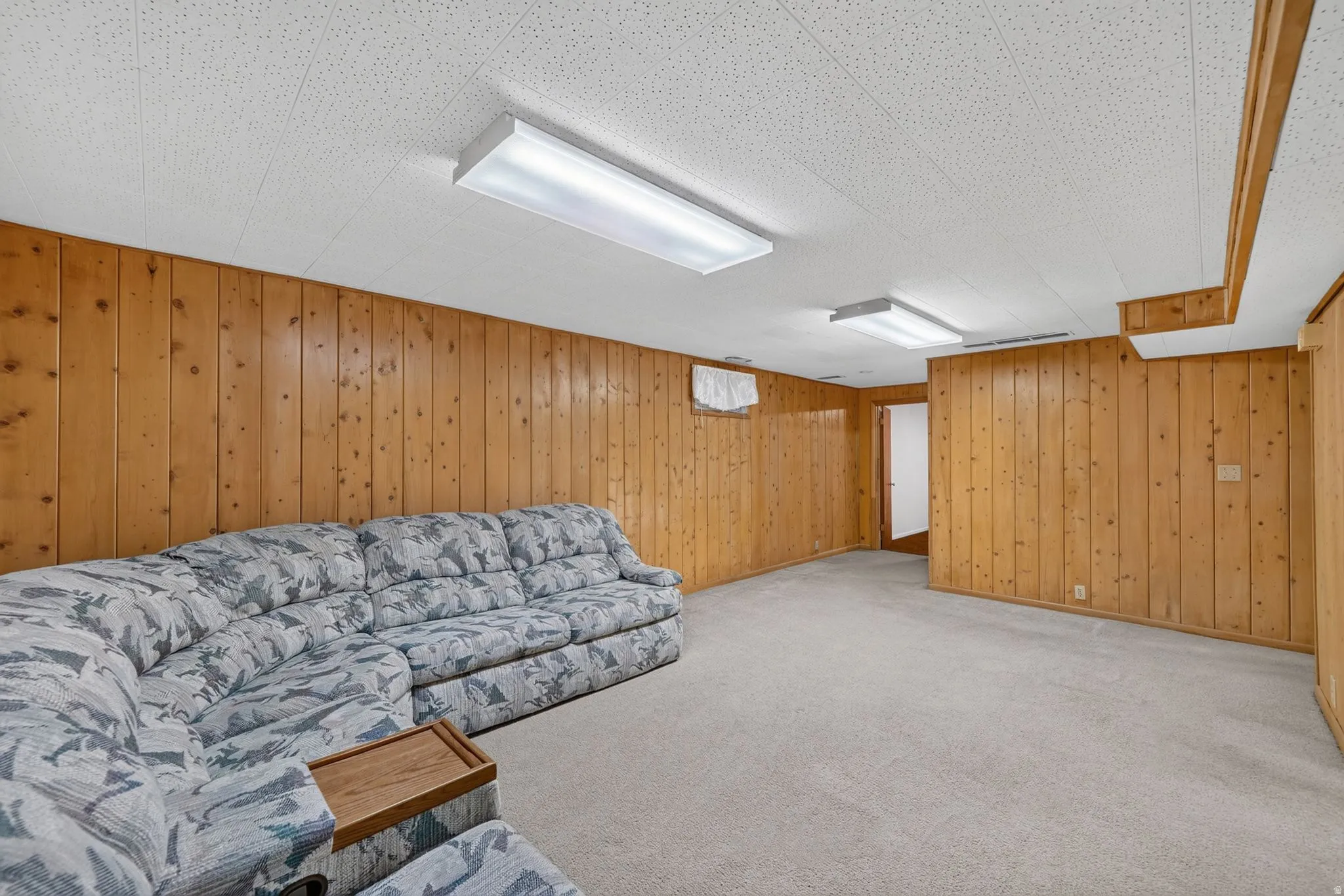 Spacious room featuring wood paneling, light gray carpeting, and acoustic tile ceiling