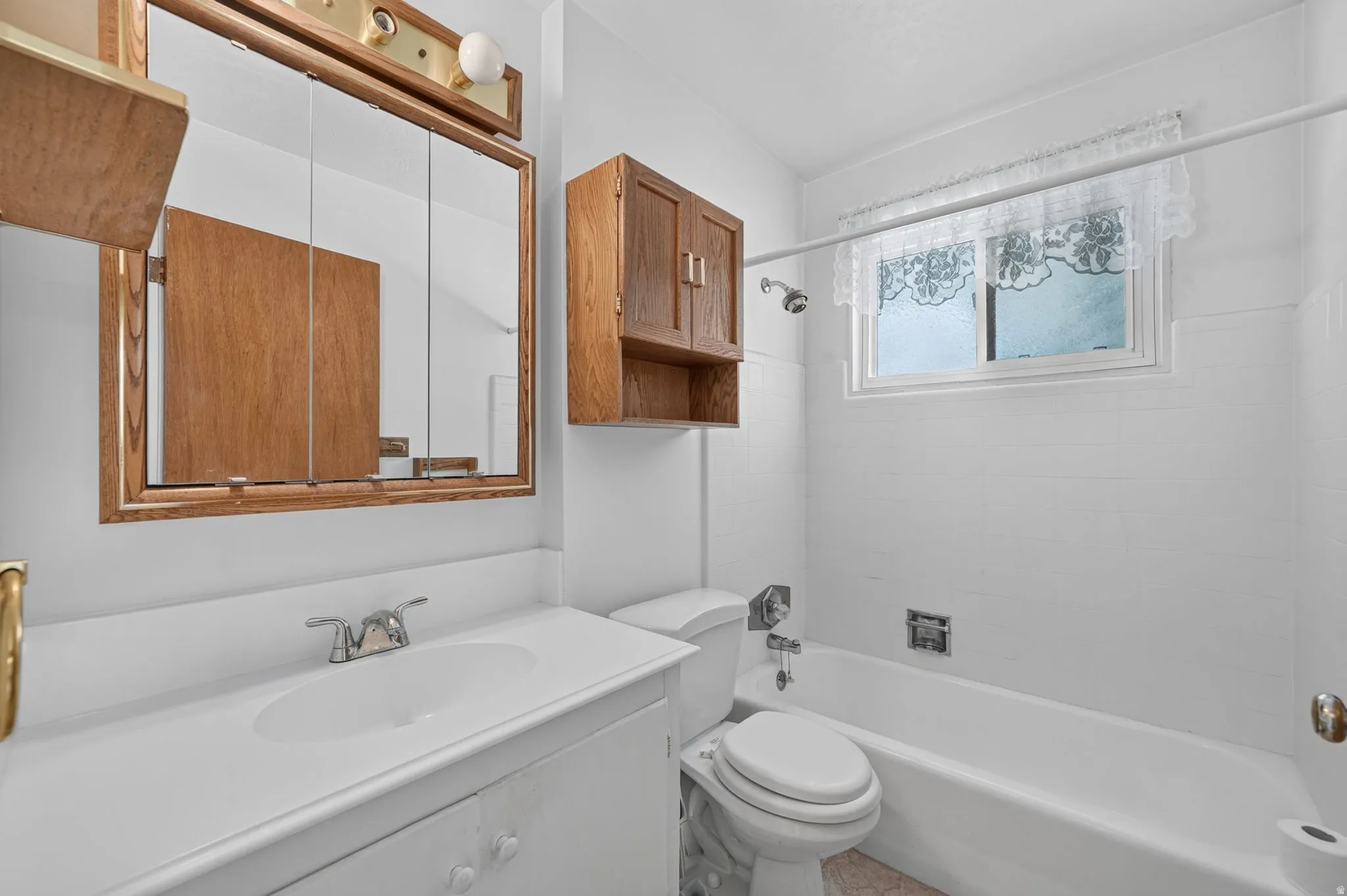 Bathroom featuring a vanity with an integrated sink, a medicine cabinet with mirror and overhead lighting, a toilet, and a bathtub with shower fixture