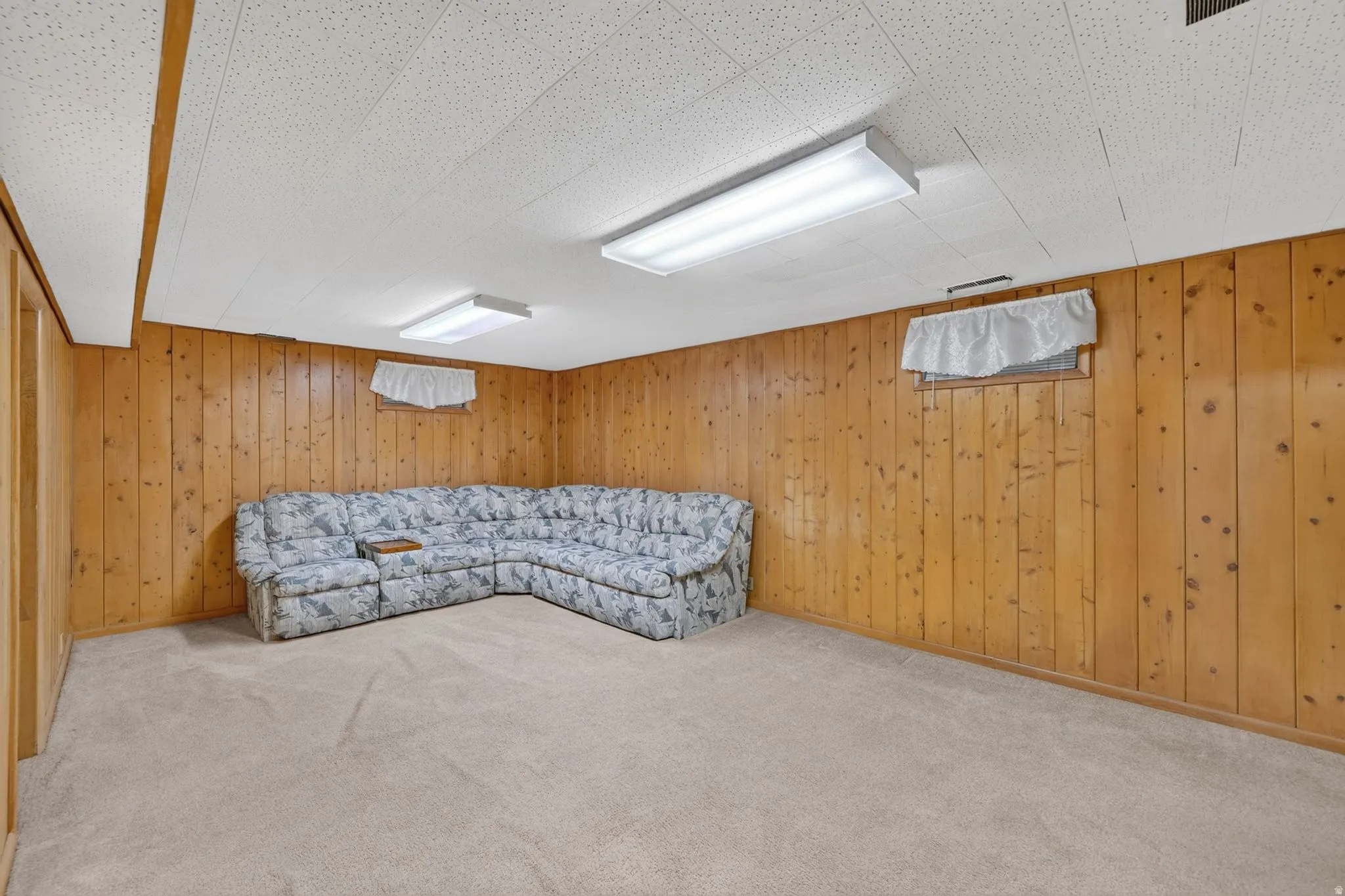Carpeted room featuring wood-paneled walls, a drop ceiling with integrated lighting, and two small windows