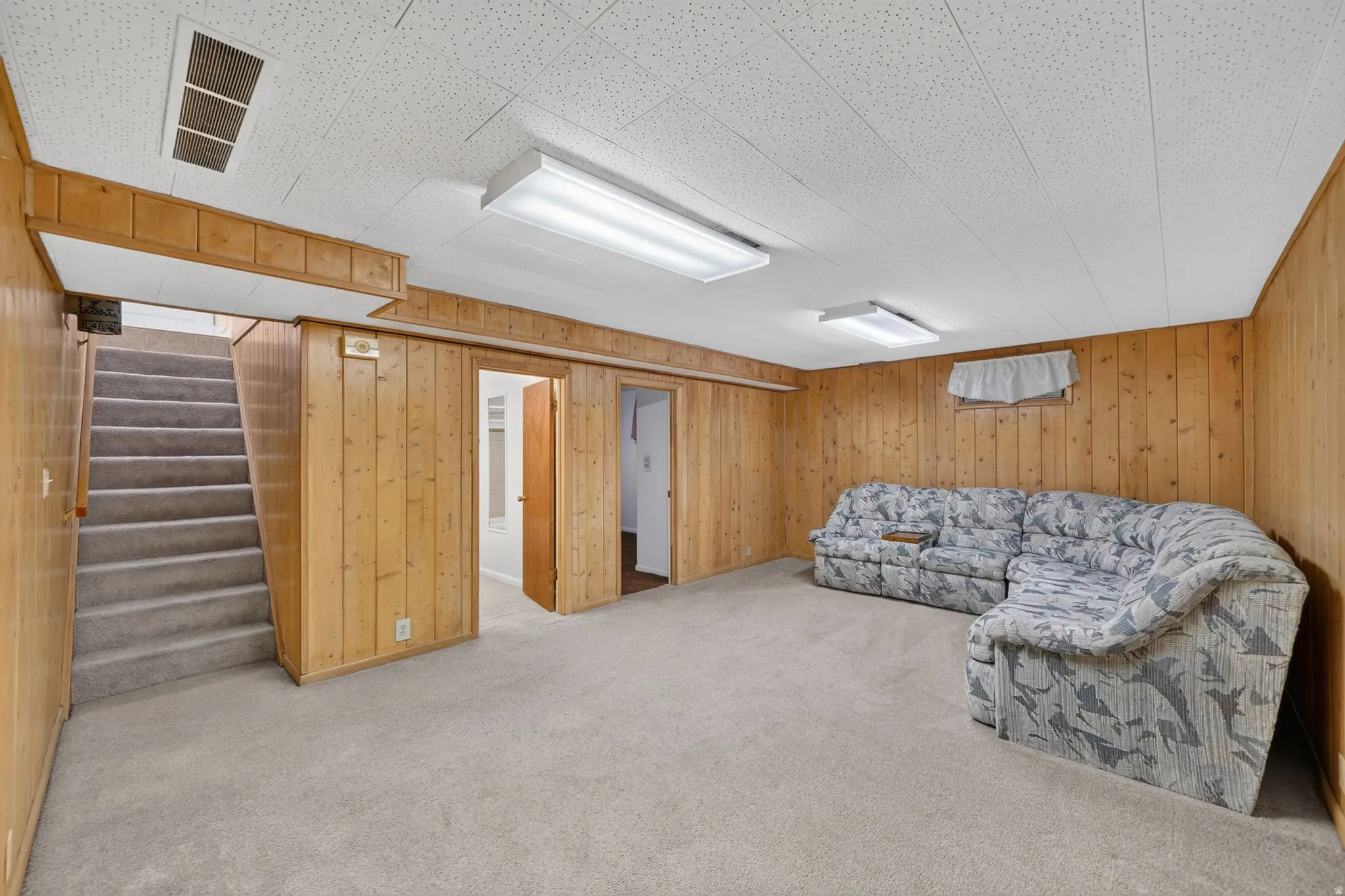 Carpeted recreation room featuring wood-panel walls, acoustic tile ceiling, and fluorescent lighting fixtures