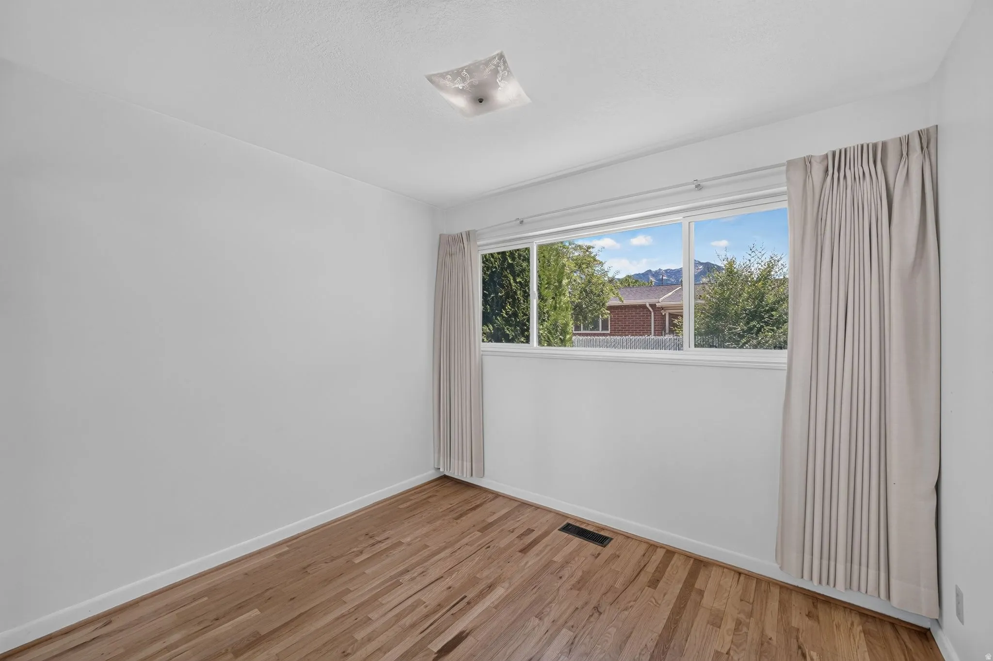 Bright room featuring wood-finish flooring, a large multi-pane window, and a flush-mount ceiling light fixture