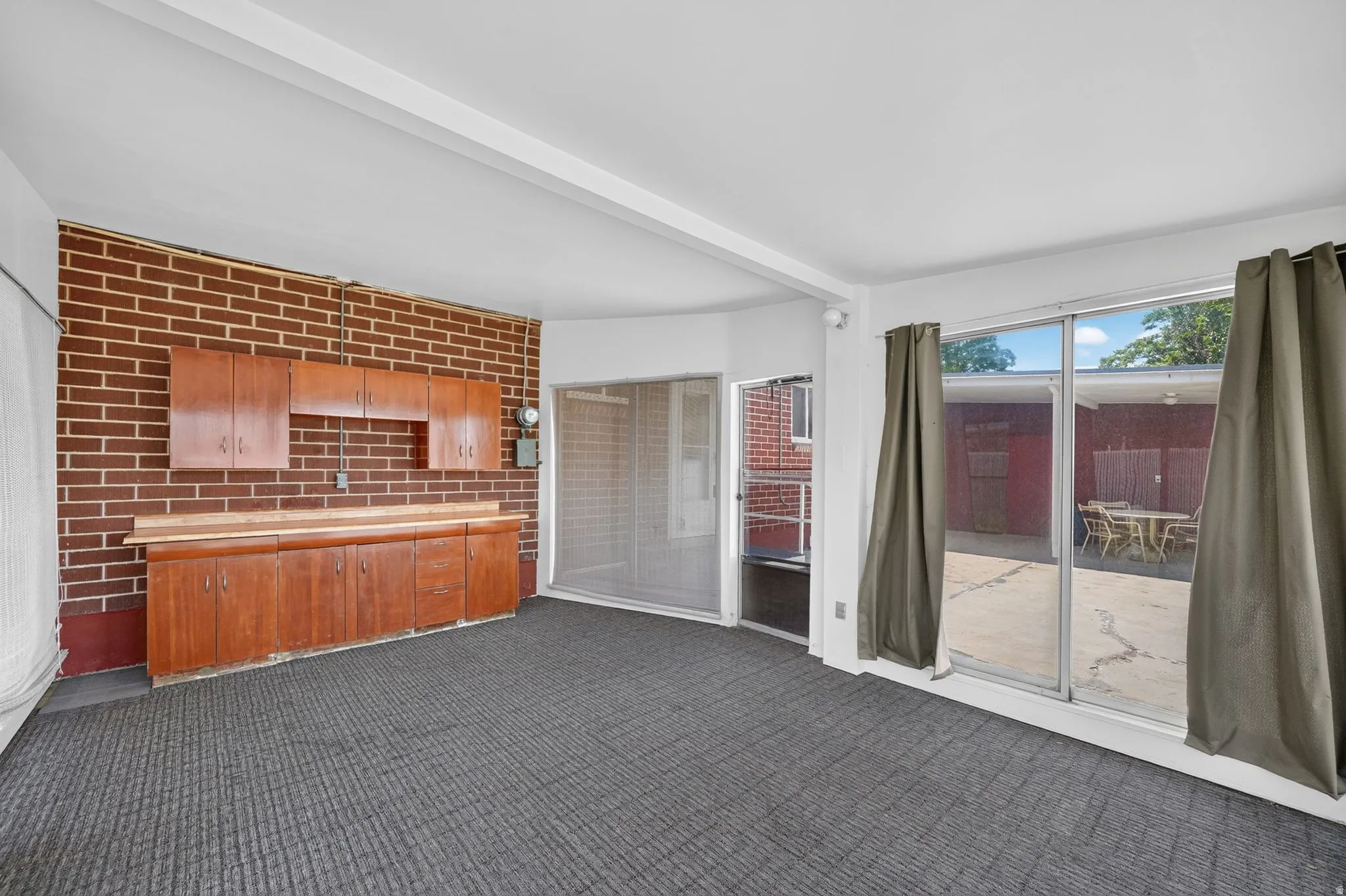 Interior space featuring brick wall accents, built-in cabinetry with wood finishes, wood-finish countertops, wall-to-wall carpeting, and large sliding glass doors providing access to an exterior patio