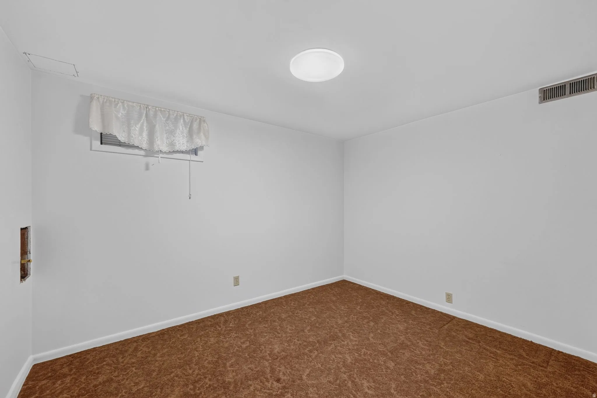 Room featuring brown patterned carpet flooring, white walls, and a ceiling-mounted light fixture