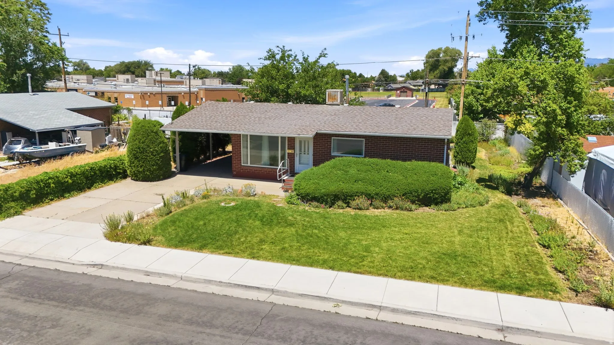Brick exterior featuring a covered carport, established front lawn, mature landscaping, and an asphalt driveway