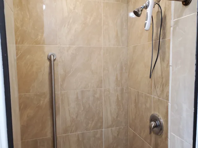 Shower enclosure with neutral-toned tiled walls, a brushed nickel grab bar, and a chrome shower fixture