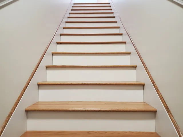 Staircase featuring wood-finish treads, white risers, light-toned wall paint, and a wood-finish handrail