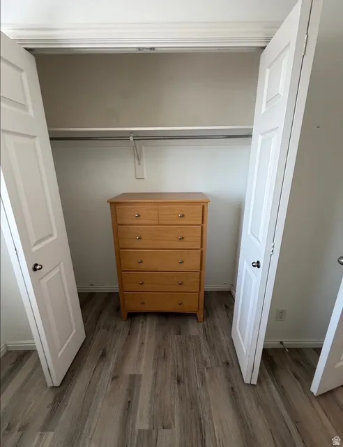 Closet space featuring wood-finish flooring, white bi-fold doors, and a built-in hanging rod