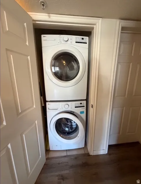 Dedicated laundry closet featuring a stacked white front-loading washer and dryer, tile flooring within the closet, and wood-finish flooring extending into the room