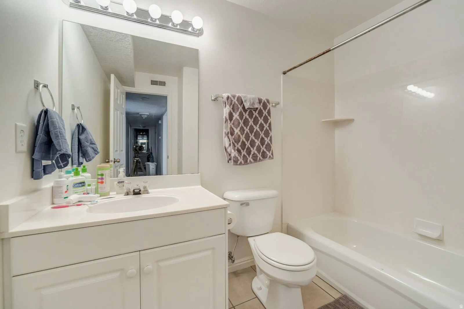 Full bathroom featuring a single vanity with storage, an integrated sink, a rectangular mirror, a four-light vanity fixture, and a combination tub and shower