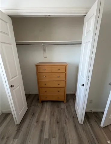 Closet space featuring wood-finish flooring, white bi-fold doors, and a built-in hanging rod