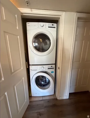 Dedicated laundry closet featuring a stacked white front-loading washer and dryer, tile flooring within the closet, and wood-finish flooring extending into the room