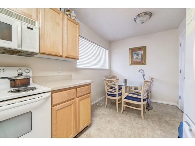 Compact kitchen space featuring light wood cabinetry, white appliances, and a window with horizontal blinds