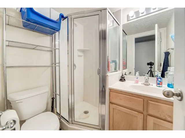 Bathroom featuring a glass-enclosed shower, single vanity with a light-toned countertop, natural wood-finish cabinetry, and contemporary vanity lighting