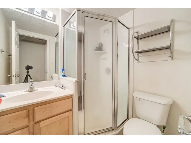 Bathroom featuring a glass-enclosed shower, a vanity with wood cabinetry and a white countertop, a mirror with strip lighting, and a white toilet