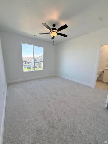 Spacious room featuring neutral carpeting, a large window, a ceiling fan with integrated lighting, and white baseboards