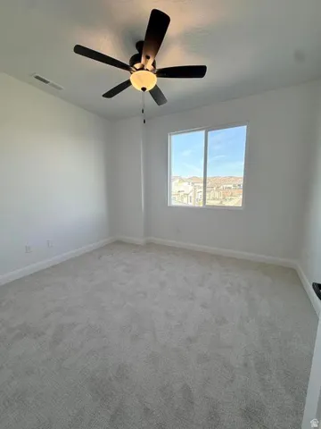 Bright room featuring a large window, plush gray carpet, clean white walls, a ceiling fan with integrated lighting, and white baseboards