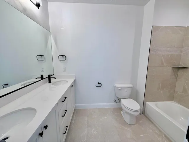 Contemporary bath featuring a dual vanity with white cabinetry and integrated sinks, matte black fixtures, an expansive wall mirror, and a bathtub with tiled surround